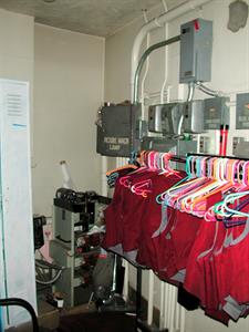 Red uniform vests hang from a rack in front of some electrical panels. On the left are some lockers painted white. - , Utah