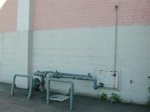 Two metal barriers, one bent, protect a gas meter, which passes through a small white door, hinged at the top. - , Utah
