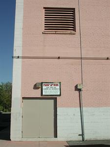 A pink brick wall with white concrete base. Double doors are at ground left, at the left edge. A sign above the door reads, 'Park at Your Own Risk.' The ventilation grill is higher on the wall and a bit right of the doors. - , Utah