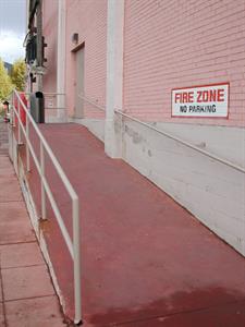An exterior shot showing the ramp, with railing on the left side and a handrail mounted to the side of the building on the right. Painted on the brick are the words, 'Fire Zone. No Parking.' - , Utah