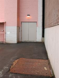 Set into the asphalt of the parking lot is a metal covering. On the right is a concrete and brick wall for the neighboring office building. In the background is the theater's southwest corner, with exit double doors and a brick chimney. - , Utah