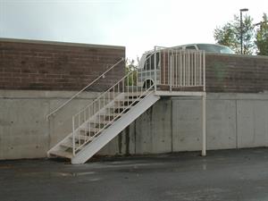 A metal staircase with railings rises from an asphalt parking lot to an opening in a brick wall. A vehicle can be seen parked on the other side of the wall. - , Utah