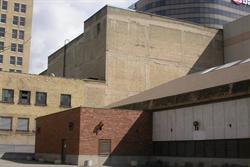 Looking towards the exterior rear wall of the Utah Theatre.  In front of the theater is a small red brick building which is connected with a larger building, whose roof slopes upwards towards the Capitol Theatre.
