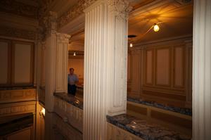 Looking southeast across the area of the mezzanine open to the lobby below. Decorative pillars divide the north wall into three openings. A man is visible in the second. Because of the angle of the shot, the third opening is barely visible. - , Utah