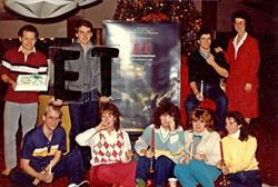 Employees pose around a poster, with one holding a cake and another the marquee letters for E. T.