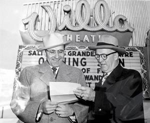 Two men stand in front of the Villa Theatre marquee, looking at a sheet of paper.  The first two lines on the attraction board read, "Salt Lake