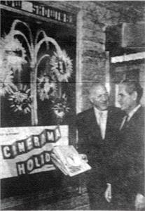 Two men stand by a poster of Cinerama Holiday, with the ticket booth in the background. - , Utah