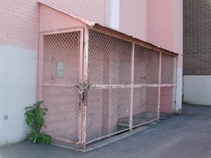 Along the rear exterior wall is an awning covering stairs to the basement. A gate at the top of the stairs is chained shut, although a section of the pink-painted chain link fencing is missing at the far end. - , Utah