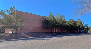 Looking across a street at a cinderblock building lined with trees.  At the far end, the roof is higher and the exterior wall stands out a bit further. - , Utah