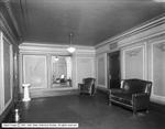 Looking from one corner of the room to the opposite corner. A couch occupies the middle of the right wall, while a sofa chair stands in the corner. A spittoon is on the floor in the lower left corner. - , Utah