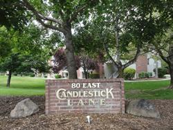 A monument sign for Candlestick Lane, with an apartment building obscured by trees.