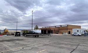Looking across the parking lot at the theater.  An office trailer stands on the right, behind temporary fencing.  A trailer, flatbed, trucks, and a CAT are on the left. - , Utah