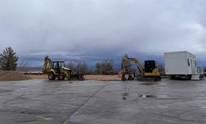 Looking across a parking lot at two CAT diggers standing at the edge of gravely area.  A construction office stands to the right. - , Utah