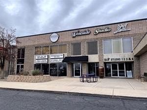 A two-story building of decorative cinderblock is set back from the curb.  A single story area juts out on the right, mostly out of the photo.  Along the top of the building are signs for Westside Studio and Spotlight Bodyworks. - , Utah