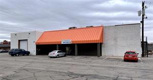 Three cars are parked in front of a white brick building. An orange-red awning covers the middle half of the building, supported by three dark pillars.