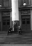 A man stands in front of a column while two men sit on the steps.  On either side of them are entrance doors of the theater. - , Utah