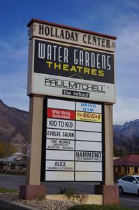 Standing next to the street is a tall sign with Water Gardens Theatres and Paul Mitchell the School at the top.  Below that, half of 16 smaller sections are in use by other businesses. - , Utah