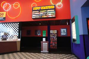 A ticket-taker's stand in the middle of the entrance to the theater hallway. Above is a 'Now Seating' sign. The light behind each title turns on when the movie is ready for seating. - , Utah