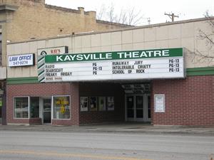 The Kaysville Theatre has red brick on the lower half, with three rows of white squares above, with a green border between.  To the left of the theater entrance are windows and doors for two stores. - , Utah