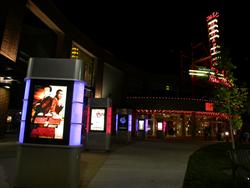 Poster cases with blue and red lights line the left side of the walkway.  On the right, a tree in the foreground partially obscures the theater's sign in the background. - , Utah