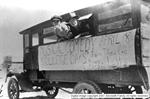 Two boys stick their heads out of a window of a long motor vehicle.  Below the windows is a hand written sign. - , Utah