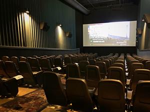 A long narrow auditorium with a center aisle and five seats on either side.  On every other row, a laminated paper sitting on the arm rest indicates the row of seating is closed. - , Utah