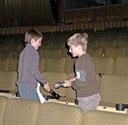 Two boys with flashlights stand in a row of seating.  The rear of the auditorium can be seen in the background and the edge of the projection window appears in the upper left. - , Utah