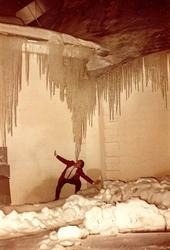 A man crouches below the point of a huge collection of icicles hanging off the edge of the roof at the rear of the lobby. - , Utah