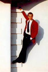 A man in a white shirt, tie, and red suite coat stands on a narrow ledge in the cinder block wall. - , Utah