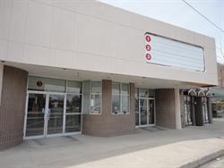 The entrance of the theater has a ticket booth, with doors on either side and an attraction board above.