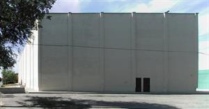 The tall exterior wall of a cinderblock building painted white. Four reinforced columns divide the wall into fifth.  Two exit doors stand just to the right of the third column from the left. - , Utah