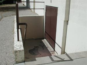 A short flight of exterior steps leads to a set of dark brown double doors on the right.  Beyond the stairwell, a path continues along the building toward the front. - , Utah