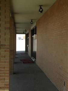 On the right is a brick wall with two sets of glass doors in the background. On the left are six brick pillars.  Four sets of lights are mounted in a white ceiling overhead.  Sunlight washes out the far end of the walkway. - , Utah
