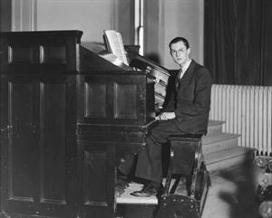 J. J. Keeler practices the organ in the College Hall Recital Hall in 1936.  The proscenium arch on the left side of the stage is visible in the top left of the photo.  Heavy velour drapes cover a windw in the top right. - , Utah