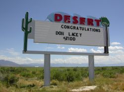 The sign of the Desert Drive-In has five-line attraction board with the word 'Desert' above and a cactus and a palm tree on either side. - , Utah