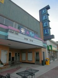 Above the entrance of the theater is a flat sign with the Reel Theatre logo and a three-line attraction board. - , Utah