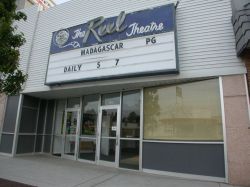 The sign for 'The Reel Theatre' is above the entrance and has a four-line attraction board.  The entrance is a diagonal wall with windows and two doors.  On the left of the entrance there may have been an ticket booth. - , Utah