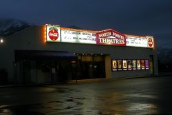 The front of the North Pointe Theatres at night.  The ticket booth is at the left of the entrance.  An attraction board with the name of the theater in the center covers the upper portion of the facade. - , Utah