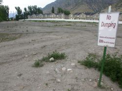 A 'No Dumping' sign stands near where the screen was located.  In the background can be seen the narrow sliver that remains of the main theater.  Homes have been built over most of the site. - , Utah