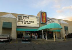 A canopy covers the walkway up to the Movies 8 ticket window.  Above the ticket booth is the theater's sign and attraction boards. - , Utah