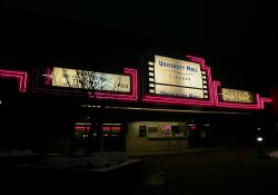 Neon around the sign and attraction board of the Festival Cinemas at University Mall at night.